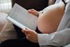 A_pregnant_person_sits_comfortably_on_a_couch,_engrossed_in_reading_a_book