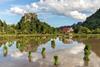 Water_reflection_of_mountains,_hut,_green_rice_sheaves_scattered_in_a_paddy_field_and_clouds_with_blue_sky_in_Vang_Vieng,_Laos