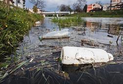 Close-up_of_plastic_bottles_polluting_the_river_with_a_bridge_and_buildings_in_a_blurry_background_(51142599174)