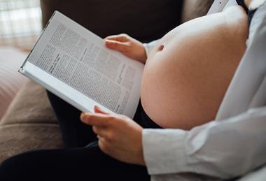 A_pregnant_person_sits_comfortably_on_a_couch,_engrossed_in_reading_a_book