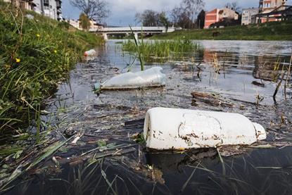 Close-up_of_plastic_bottles_polluting_the_river_with_a_bridge_and_buildings_in_a_blurry_background_(51142599174)