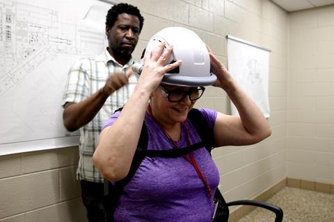 Clack stands behind Chaidez with a hand to the back of the helmet, which resembles a white hard hat, as Chaidez holds it at the sides.