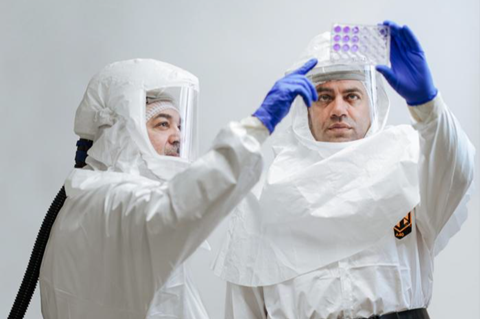 Two scientists in protective clothing examine vials of fluid