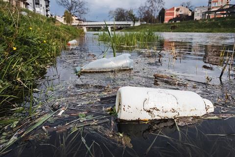 Close-up_of_plastic_bottles_polluting_the_river_with_a_bridge_and_buildings_in_a_blurry_background_(51142599174)