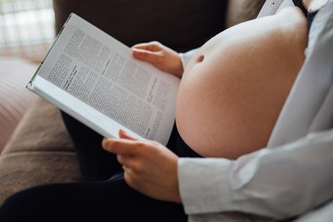 A_pregnant_person_sits_comfortably_on_a_couch,_engrossed_in_reading_a_book